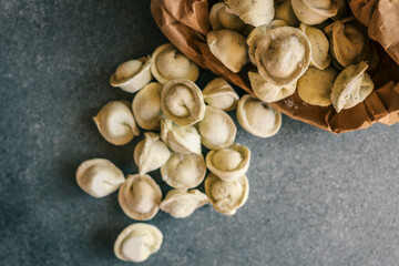 Frozen tortellini pasta spilling out of a brown paper bag onto a dark stone surface, ready for cooking or packaging