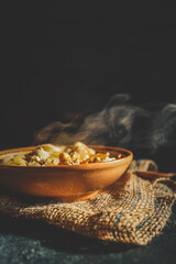 Traditional dumplings served in a rustic clay bowl with fried onions and steam rising, placed on burlap fabric in warm, moody lighting