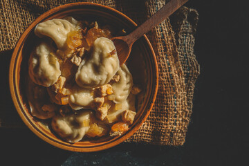 Top view of traditional dumplings served with fried onions and meat in rustic ceramic bowls, placed on burlap and a wooden board