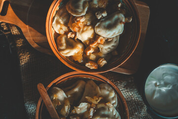 Top view of traditional dumplings served with fried onions and meat in rustic ceramic bowls, placed on burlap and a wooden board