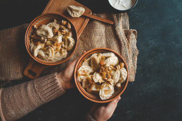 Traditional dumplings served with fried onions and meat in ceramic bowls on burlap with a bowl of sour cream and hands holding one of the dishes