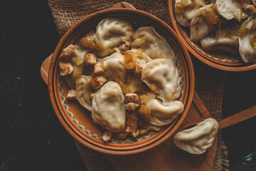 Rustic presentation of dumplings with fried onions and meat in ceramic bowls, served on burlap with one dumpling on a wooden spoon in the foreground