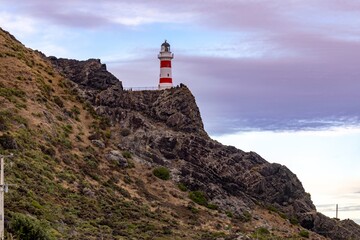 Cape Palliser Lighthouse stands tall on a rocky cliff, guiding ships along the rugged coastline of...