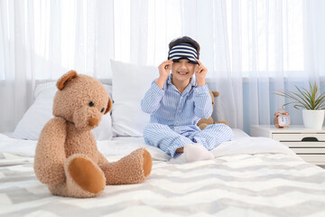 Cute happy little boy with toys and sleeping mask in bedroom