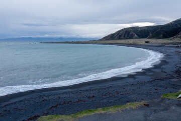 Scenic view of a black sand beach in Ngawi, Cape Palliser, Wellington, New Zealand. Waves crash on...