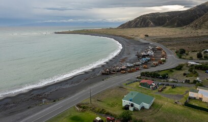 Boats and tractors line the black sand beach at Ngawi, Cape Palliser, Wellington, New Zealand. The equipment is used by local fishermen to launch their boats into the Tasman Sea.