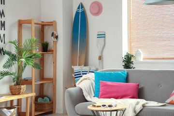 Interior of stylish living room with shelving unit, surfboard and grey sofa