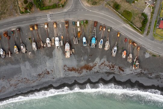 Aerial view of boats and tractors parked on a black sand beach in Ngawi, Cape Palliser, Wellington, New Zealand. The boats are being stored for the off-season, protected from the ocean waves.