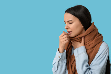 Beautiful young woman in scarf suffering from sore throat on blue background