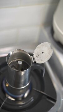 Metal moka pot brewing coffee on a gas stove with the lid open, in a cozy kitchen setting.