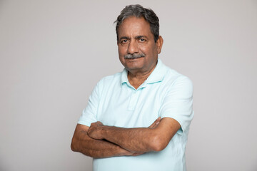 Portrait of an indian happy senior elderly man face with arm crossed isolated on grey background....