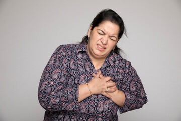  Indian matured woman holding chest with pained expression on grey studio background. Possible...