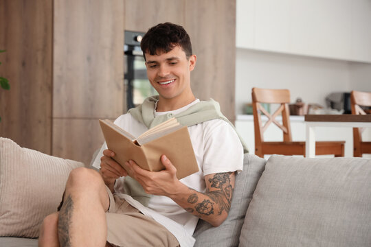 Young man reading book on sofa at home
