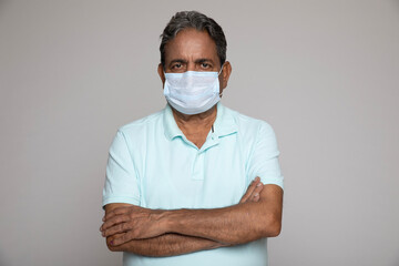 Indian arm crossed senior man wearing protective face mask against coronavirus isolated in white...