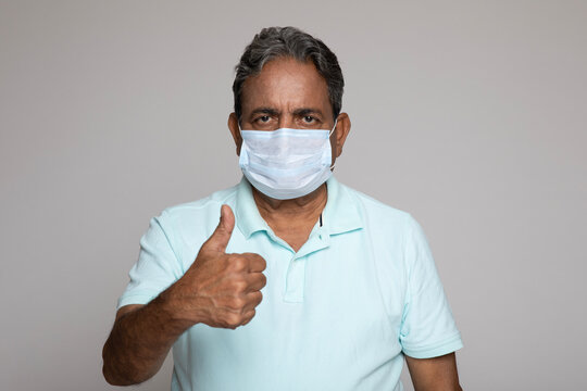 Indian senior man wearing protective face mask against coronavirus Covid 19 showing thumbs up isolated in white background. Pandemic medical concept - Powered by Adobe