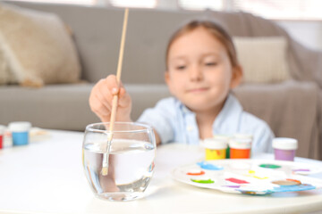 Cute little girl soaking paint brush in water at home, closeup