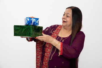 Indian beautiful senior woman holding gift boxes, standing isolated over white background. wearing...