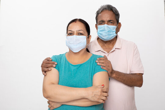 Portrait of senior couple standing with folded arms wearing blue face masks isolated on grey studio background