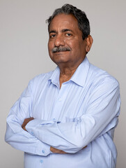Portrait of an indian happy senior elderly man face with arm crossed isolated on grey background....
