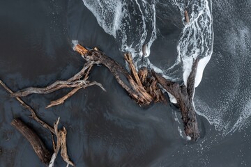 Aerial view of driftwood scattered on a black sand beach in Mokau, Waikato, New Zealand. Waves...