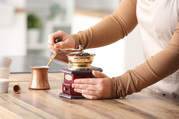 Female hands grinding coffee beans with grinder on table in kitchen
