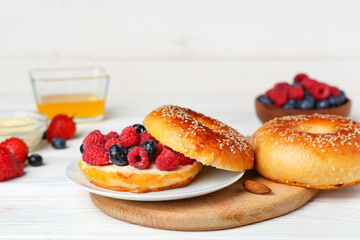 Plate of tasty bagel with butter and berries on white wooden background