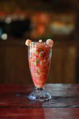 Fresh ceviche served in a tall glass on a rustic wooden table. Bright colors, natural light, no people, focus on the dish.
