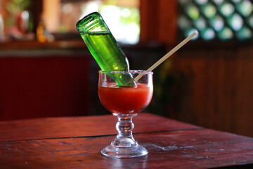 Michelada served in a tall glass with tomato juice and an inverted beer bottle. Rustic tropical bar...