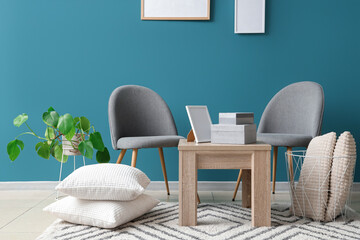 Chairs, pillows on floor, coffee table with boxes and frame near blue wall in room