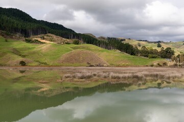 Fototapeta premium Scenic view of a lake reflecting the surrounding hills and forest in Taharoa, Waikato, New Zealand. The landscape showcases the natural beauty of the country.