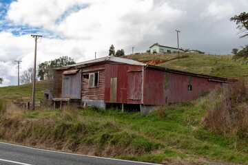 Dilapidated red corrugated iron shed sits on a grassy bank in rural Taharoa, Waikato, New Zealand....
