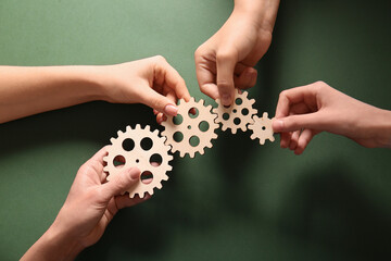Hands holding wooden gears on green background, top view