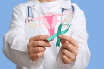 Female doctor holding turquoise ribbon with paper uterus on blue background, closeup. Cervical...