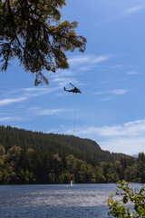 helicopter scooping water with a bucket from a mountain lake in spring or summer for a forest fire