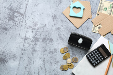 House shaped figurines with money, notebook and calculator on grey grunge background. Rent concept