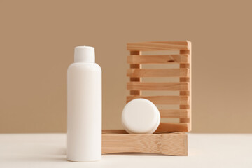 Wooden stands, jar and bottle with cosmetic products on beige background