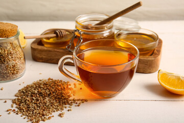 Glass cup of hot buckwheat tea with lemon and bowls of honey on white wooden background