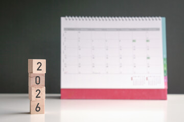 2026 on square wooden blocks stacked up. Table calendar at the background. New year new planning...