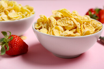 Bowl with tasty cornflakes and strawberry on pink background, closeup