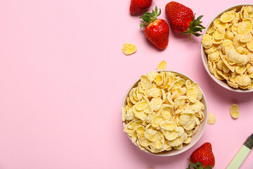 Bowls with tasty cornflakes and strawberry on pink background