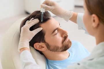 Doctor applying serum for hair growth on man's scalp in clinic