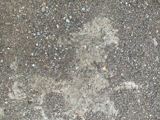 Textured Gravel and Grime Ground. An overhead shot of a rough surface composed of dark gravel with lighter patches of dirt and grime, creating an abstract pattern