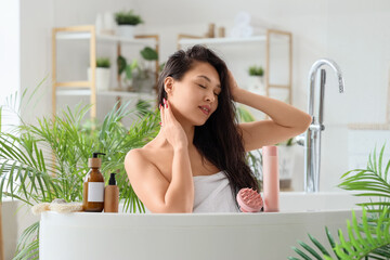 Pretty young Asian woman washing hair in bathroom