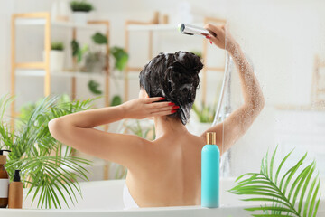 Pretty young Asian woman washing hair in bathroom