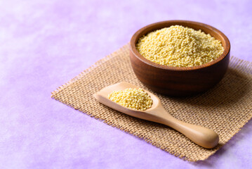 Yellow millet grain in wooden bowl with scoop on purple background, Food ingredient