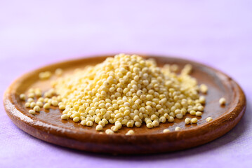 Yellow millet grain on wooden plate with purple background, Food ingredient