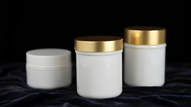 Three white jars with gold lids on a dark velvet background