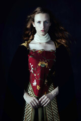 A red-haired Renaissance woman wearing an embroidered silk ensemble against a studio backdrop