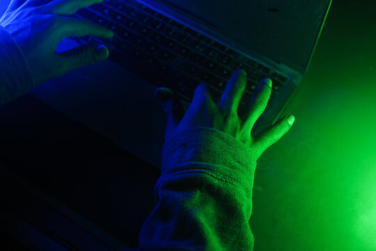 Hands typing on a keyboard in a dimly lit room, cyber crime concept 