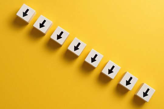 Downward trend arrow cubes on a bright yellow surface